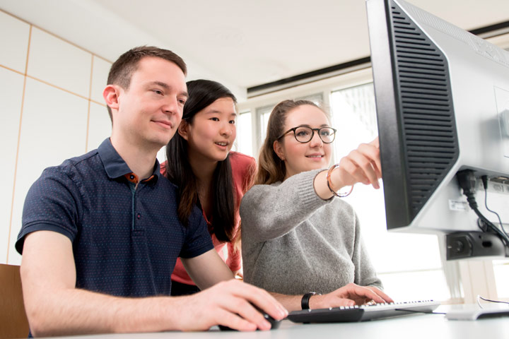 Drei Studierenden sitzen vor einem Bildschirm