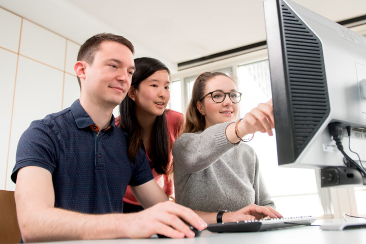 Three studens are sitting in front of a screen