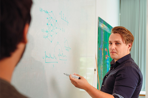 A scientist stands in front of a whiteboard and discusses a formula